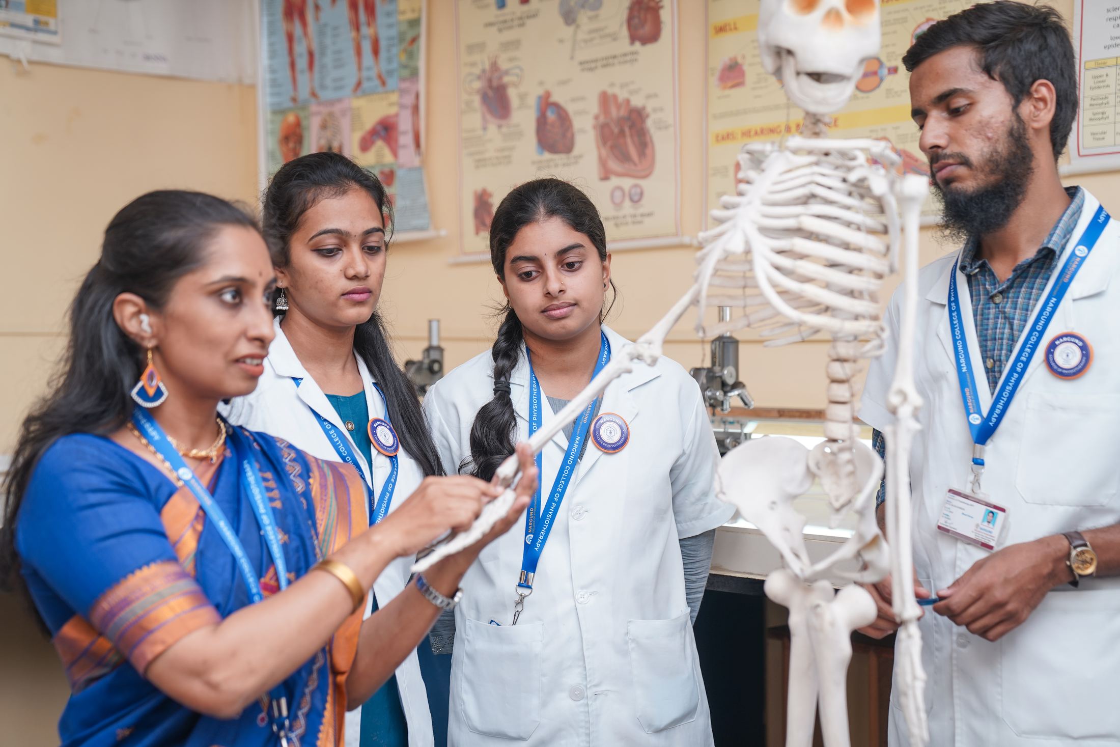 A lecturer teaching physiotherapy students with an anatomical skeleton